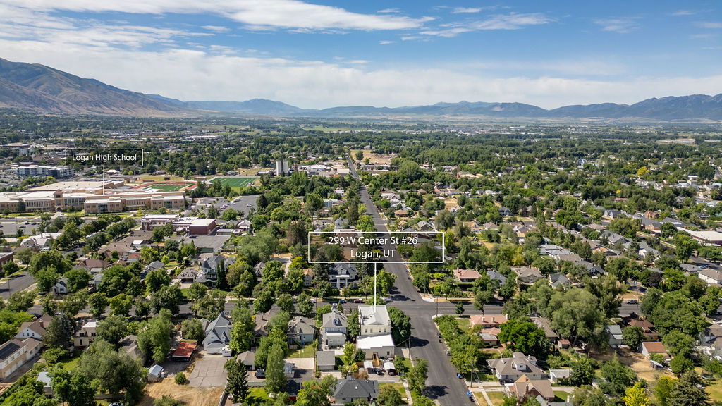 Aerial perspective showcasing a residential and commercial area with abundant mature trees, mountain ranges in the distance, and prominent buildings