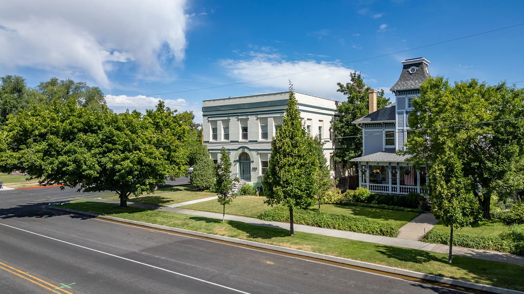 Historic-style residence featuring a prominent turret, covered porch with white railing, and a mature tree-lined street frontage