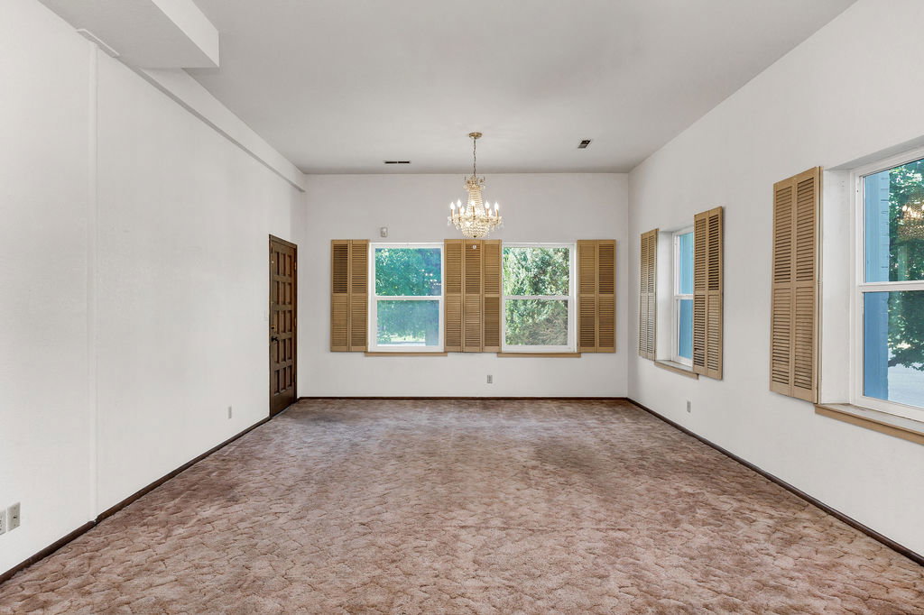 Spacious interior room featuring multiple windows with louvered shutters, a paneled door, and a chandelier