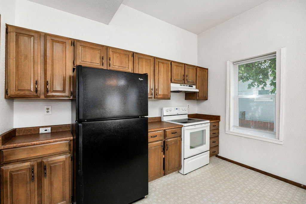 Kitchen featuring ample wood cabinetry, laminate countertops, a built-in range hood, an electric range, and a window