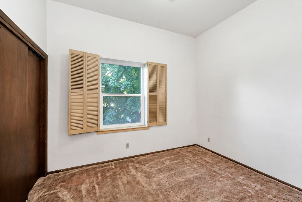 Room featuring a window with louvered shutters, white walls, and brown carpeting