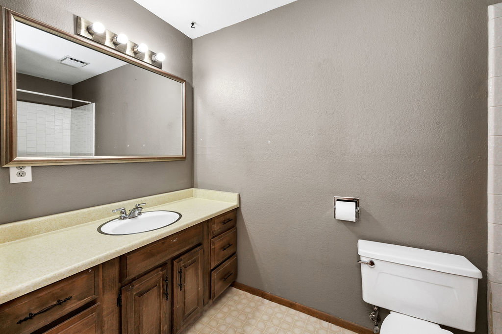 Bathroom featuring a wood-finish vanity with an oval sink, an expansive framed mirror, and a wall-mounted light fixture