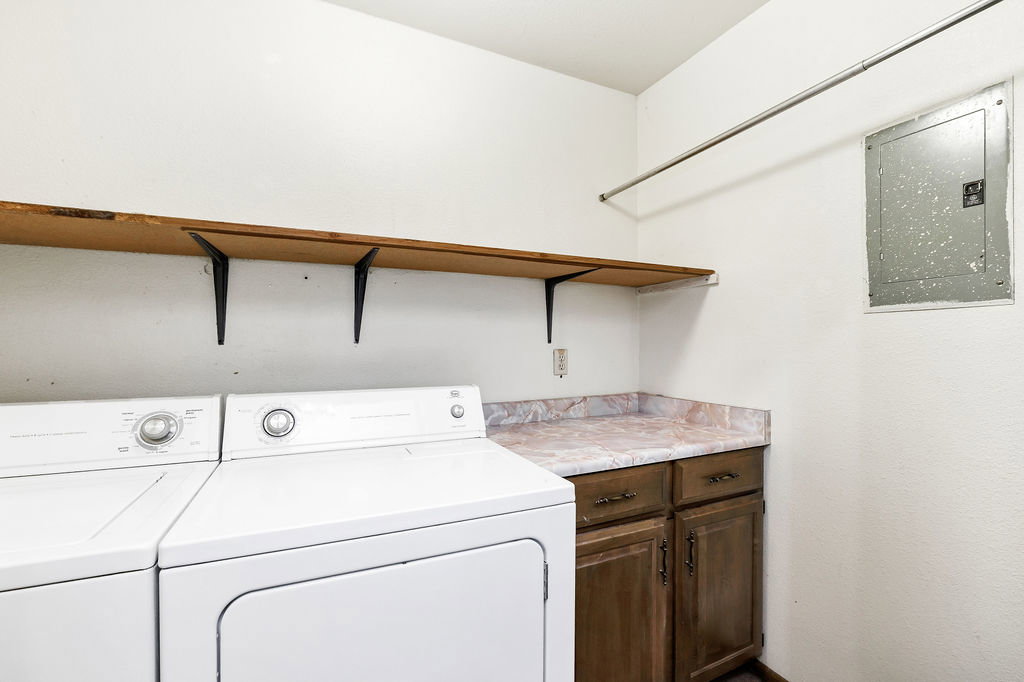 Dedicated laundry area featuring a wood-finish shelf, hanging rod, wood-finish cabinetry, and a marbled countertop