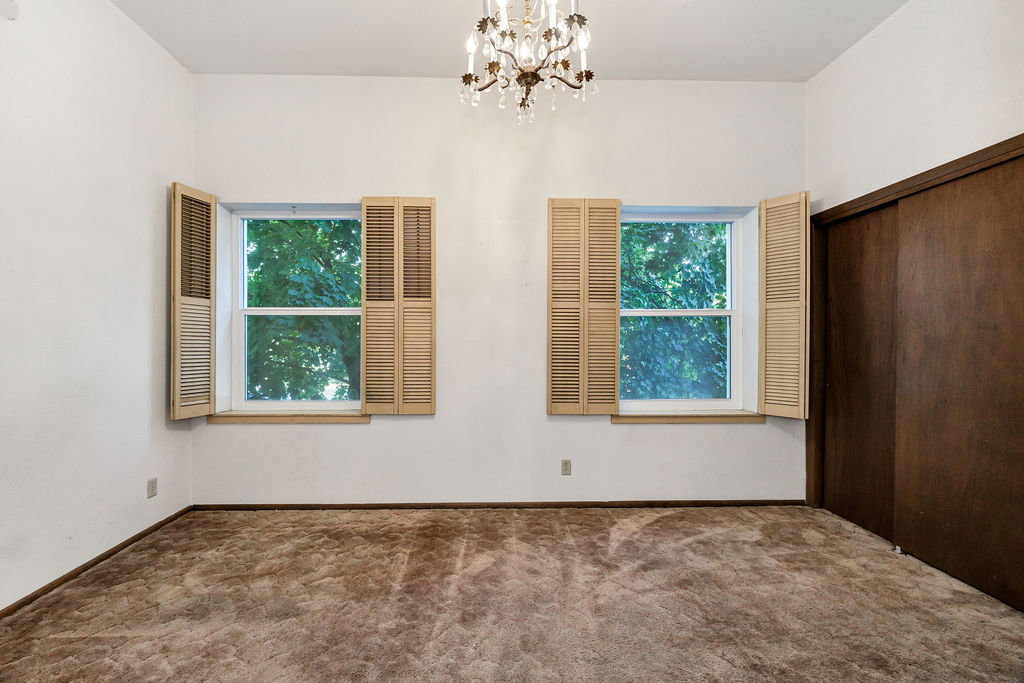 Room featuring two windows with louvered shutters, a built-in closet with dark wood sliding doors, and a decorative chandelier