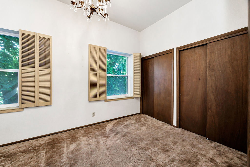 Bright room featuring two windows with louvered shutters, a crystal chandelier, and two spacious sliding-door closets with wood-finish doors