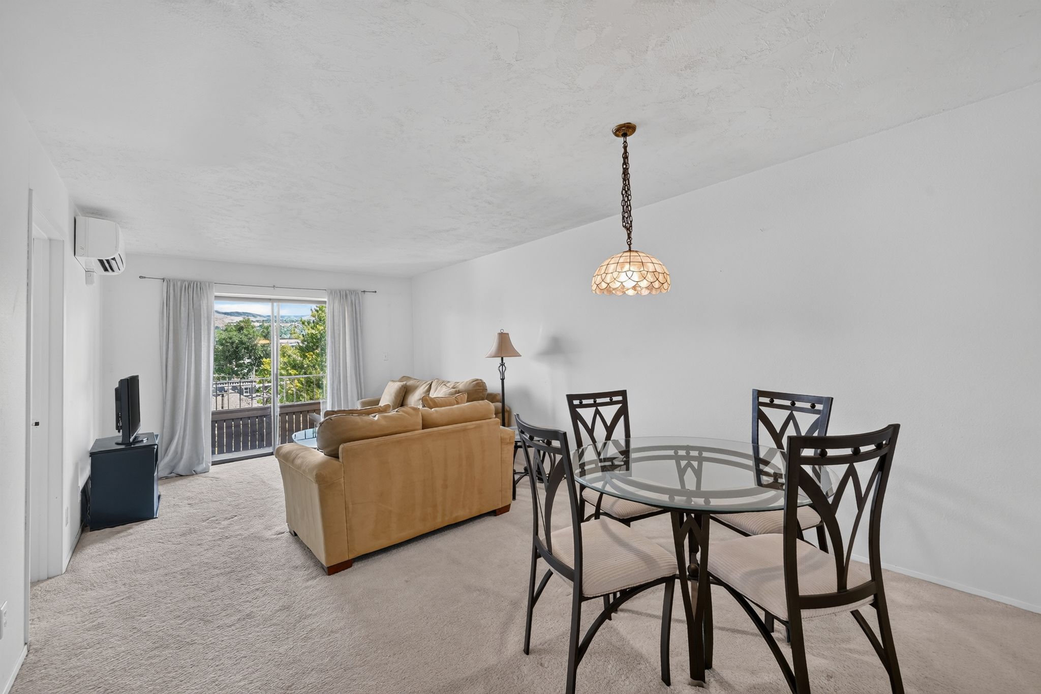 Open-concept living area with neutral carpeting and a glass-top dining table