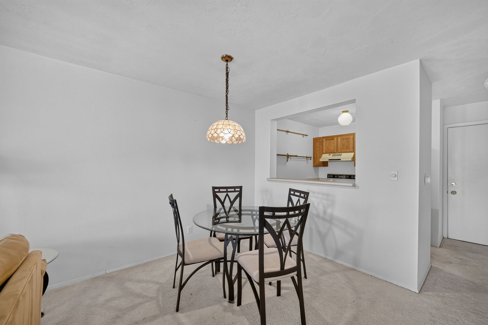 Dining area featuring a decorative pendant light fixture, carpet flooring, and a pass-through window opening to the kitchen