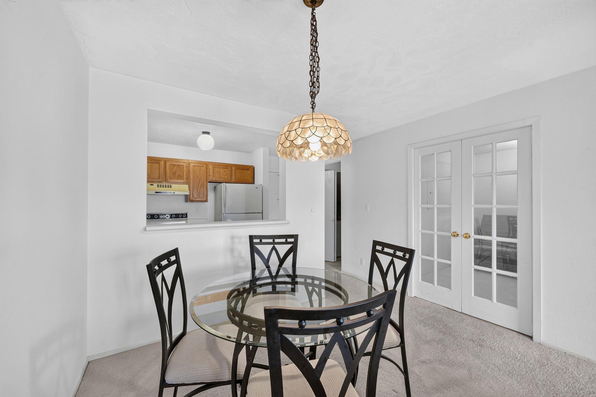 Dining area featuring a decorative shell-design chandelier, light-toned carpet, and white paneled French doors