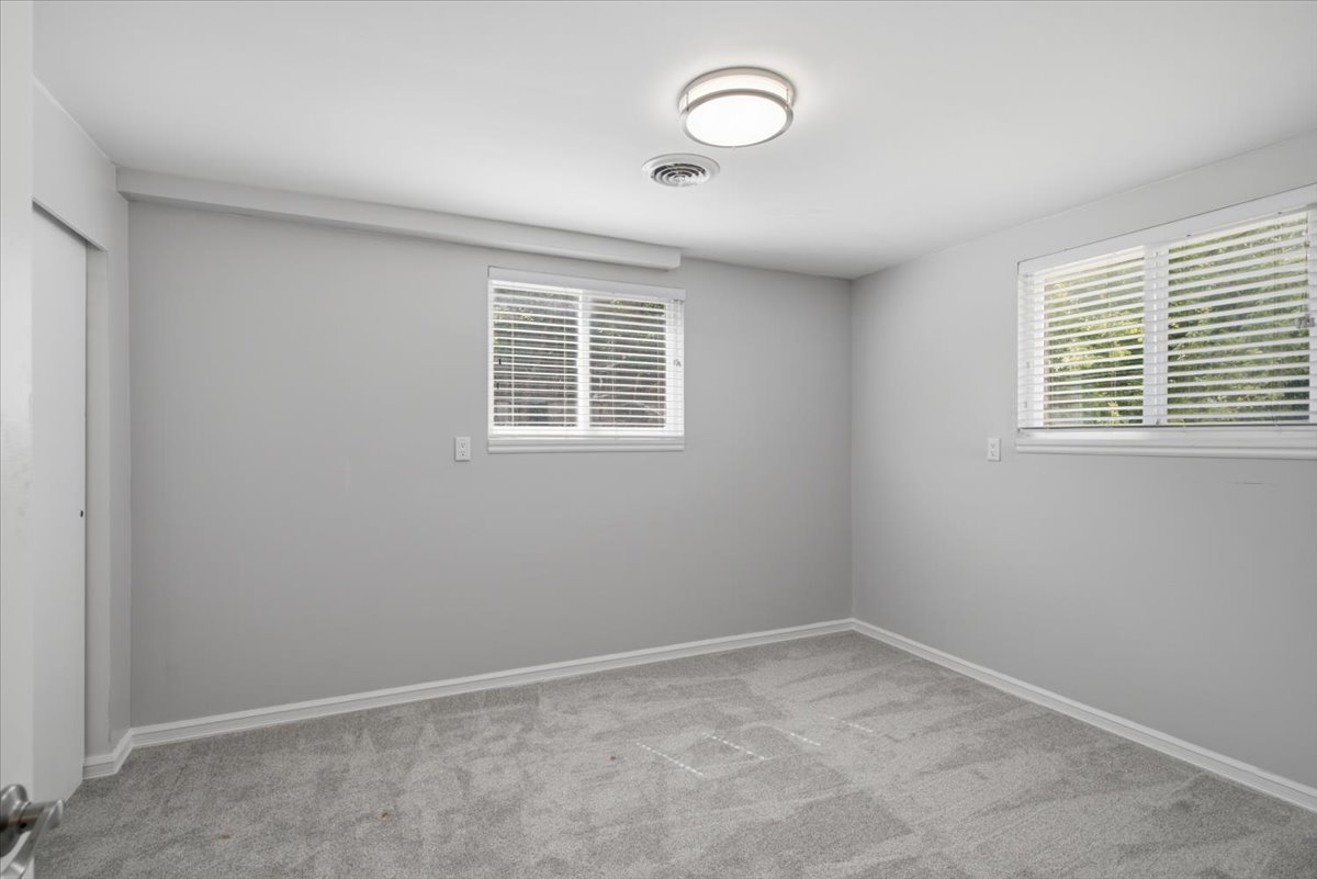 Room featuring light gray carpeting, two windows with white blinds, and white baseboards