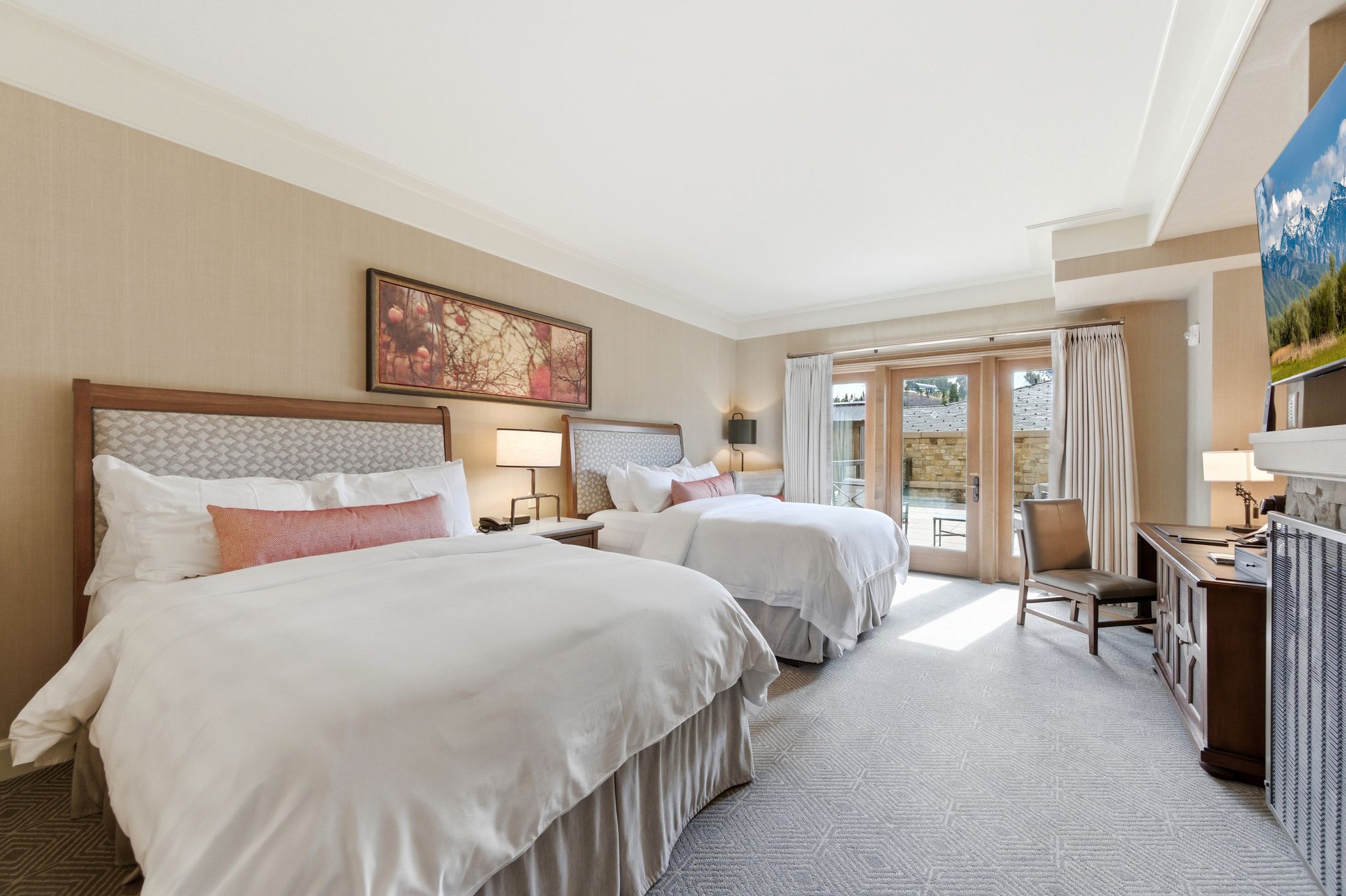 Bedroom featuring two beds with upholstered headboards, French doors opening to an exterior area, neutral-toned walls, and geometric pattern carpeting