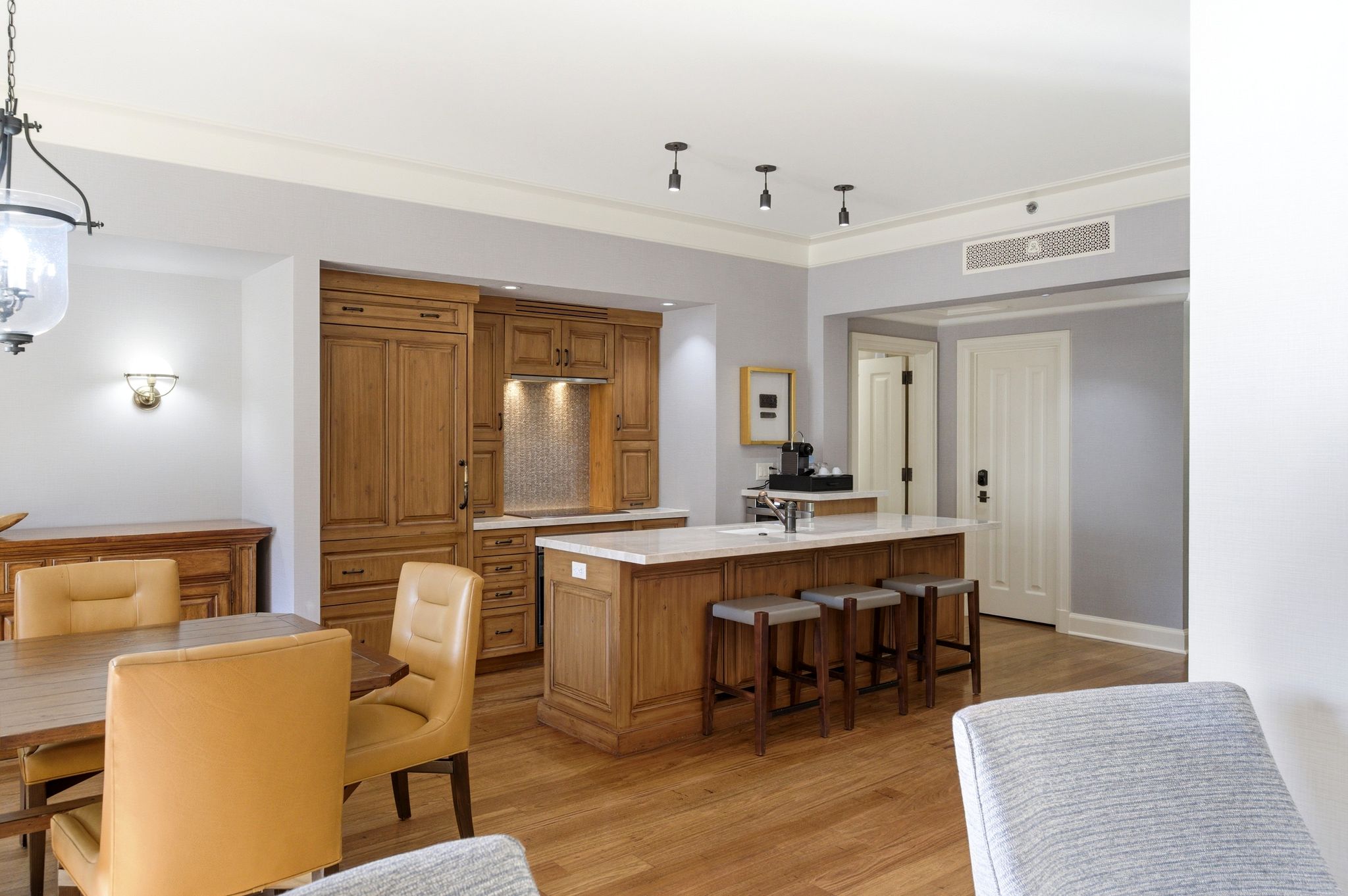 Kitchen island with a white countertop and seating for three, flanked by custom wood cabinetry featuring integrated appliances and a tiled backsplash