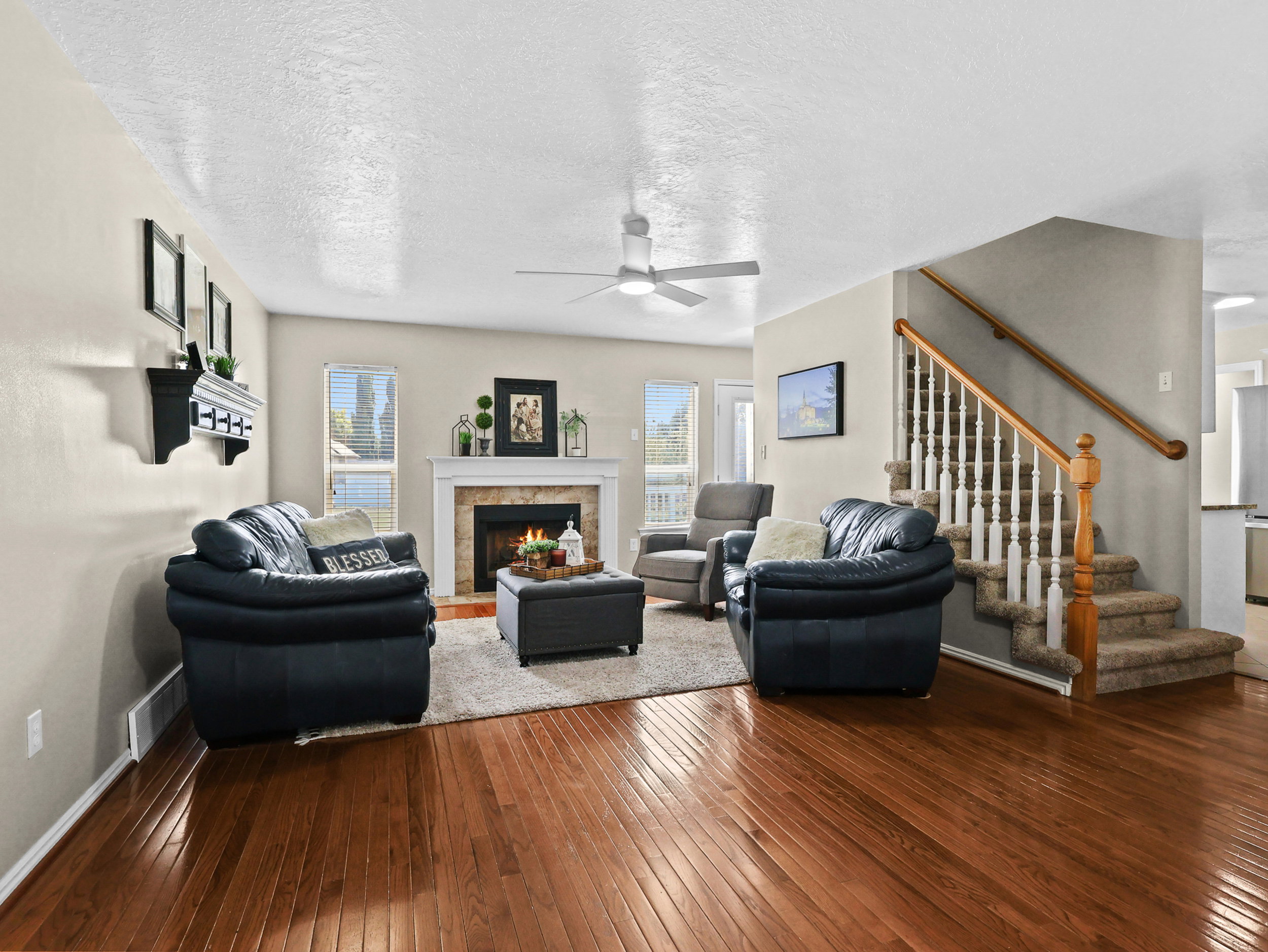 Spacious living area featuring wood-finish flooring, a fireplace with a white mantel, and multiple windows