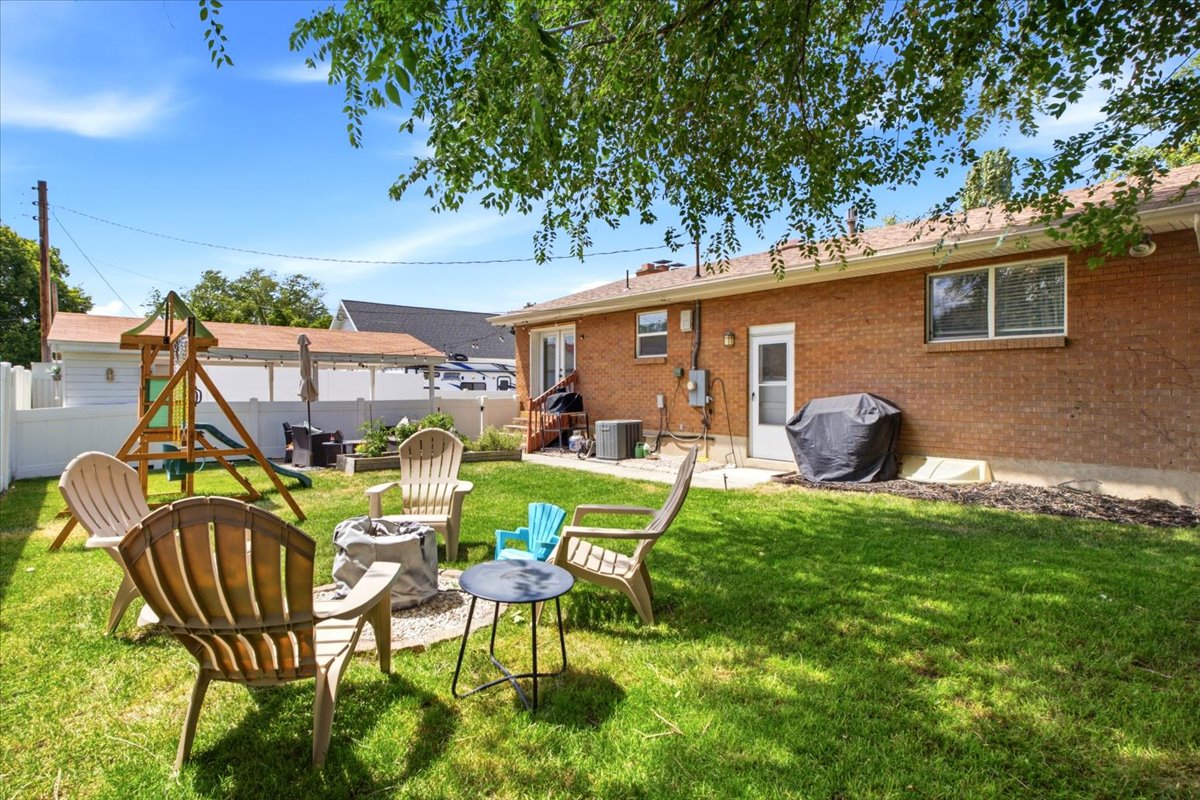 Expansive backyard featuring a lush lawn, a fire pit area with gravel surround, and a wooden playset