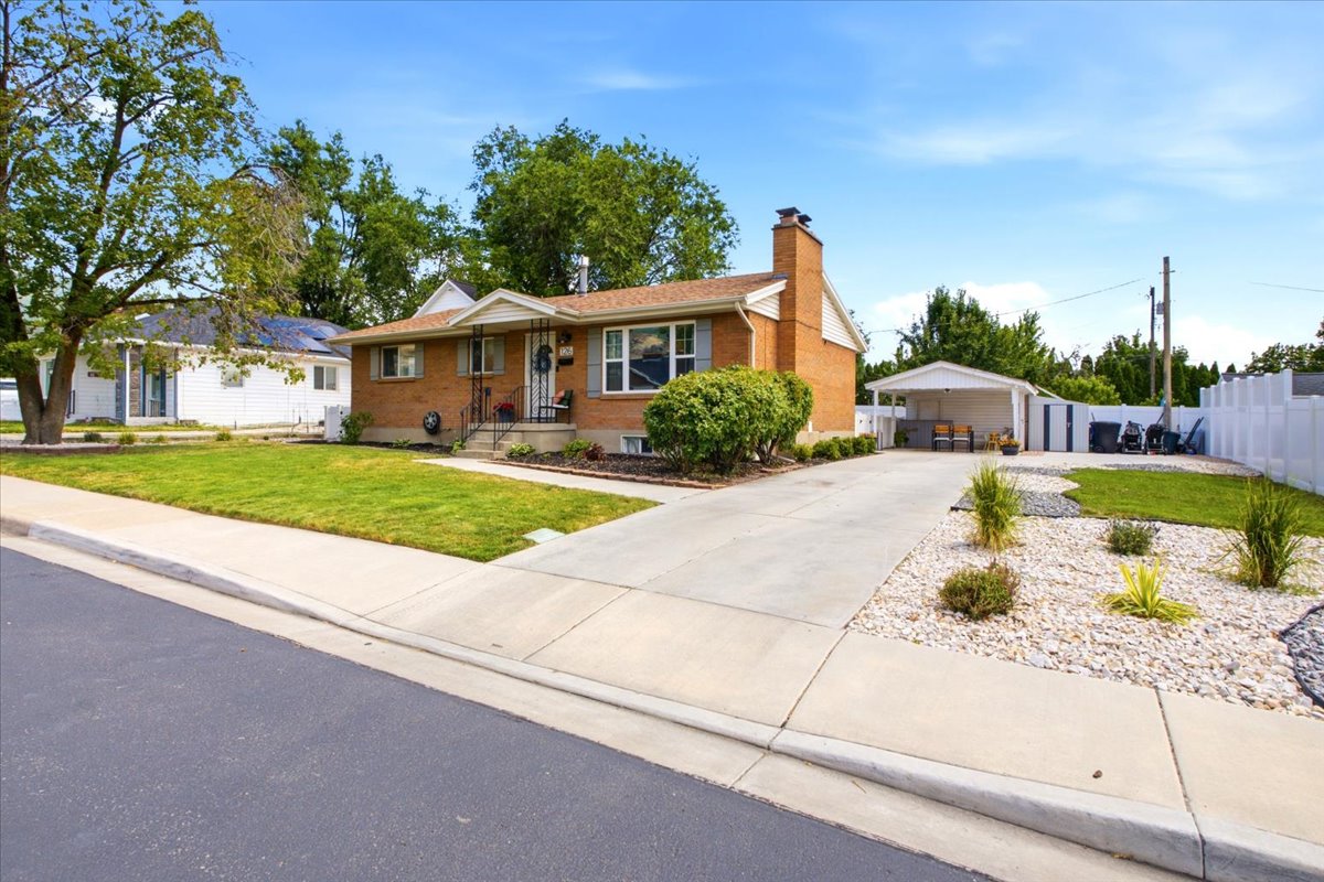 Brick exterior home featuring a concrete driveway, attached carport, and a white privacy fence