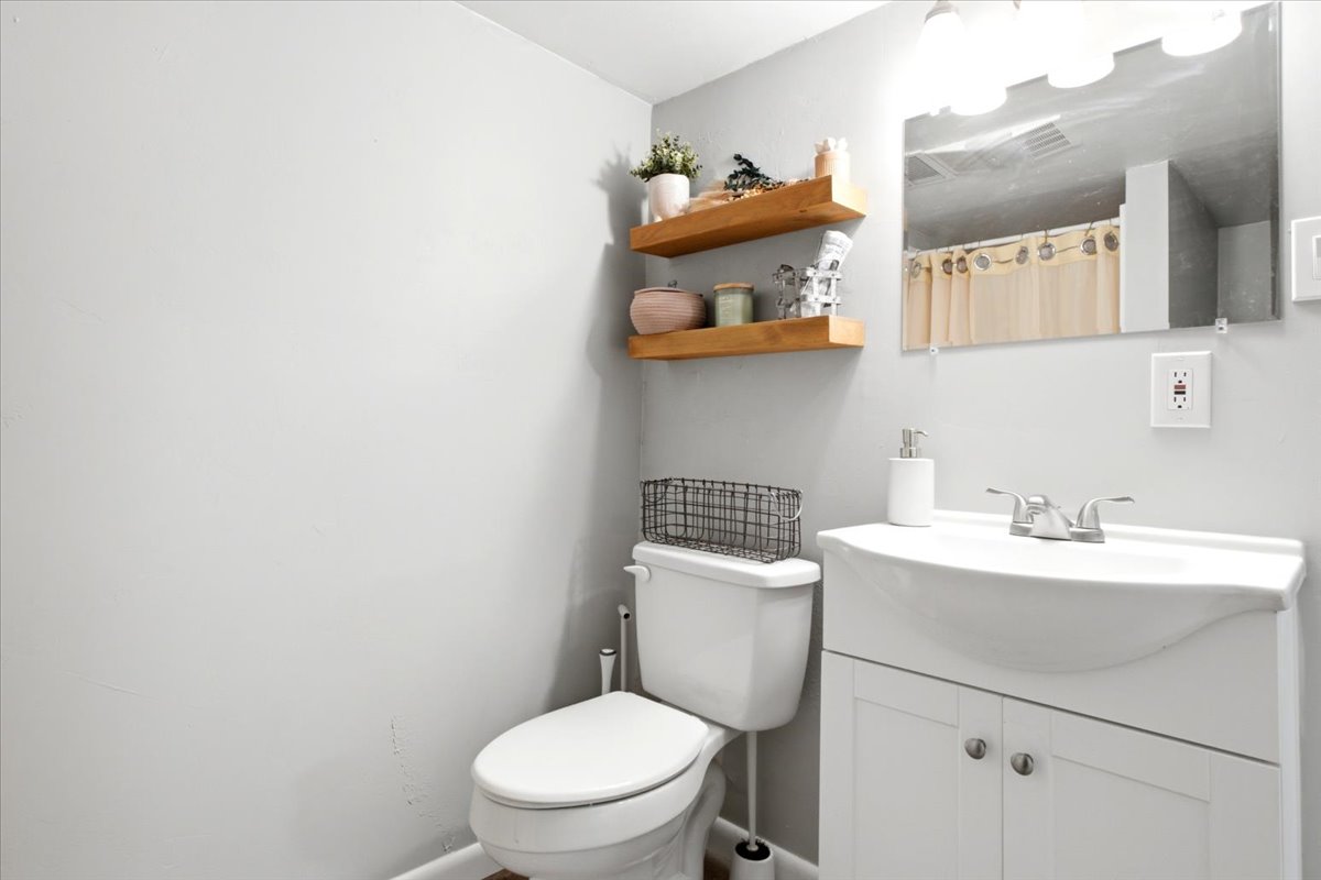 Bathroom featuring a white vanity with integrated sink, chrome faucet, wall-mounted mirror, and overhead vanity lighting