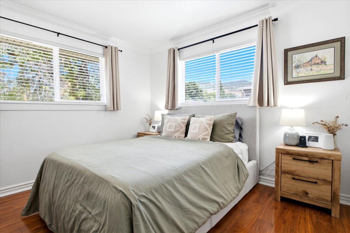 Bedroom featuring two windows with horizontal blinds, polished wood-finish flooring, white baseboards, and crown molding
