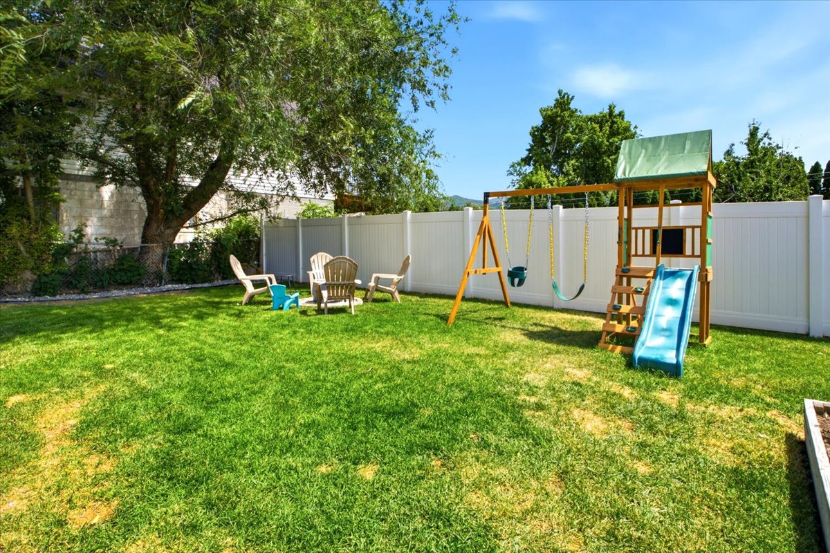 Expansive grassy backyard featuring a white privacy fence, mature trees, and a raised garden bed