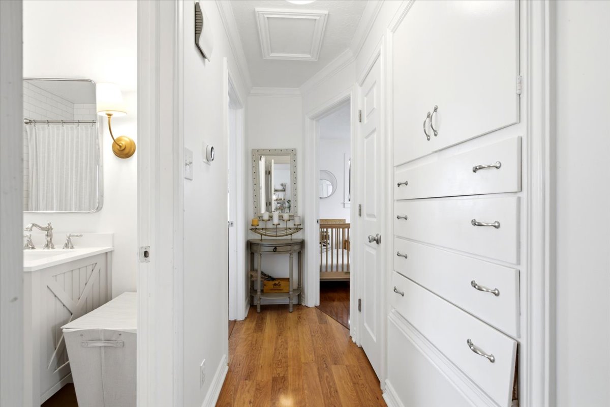 Hallway featuring hardwood flooring, white built-in cabinetry with silver hardware, and crown molding