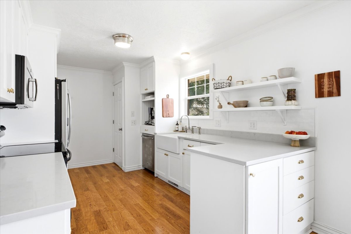 Bright kitchen featuring white cabinetry, light wood-finish flooring, white countertops, a large single-basin sink, and open shelving
