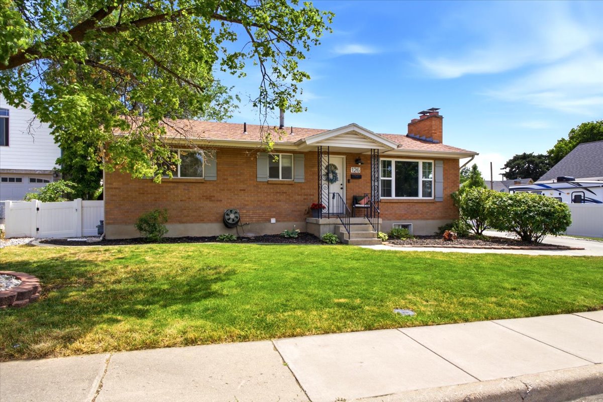 Brick exterior residence featuring a covered front porch, a mature front yard tree, a paved driveway, and a white picket fence