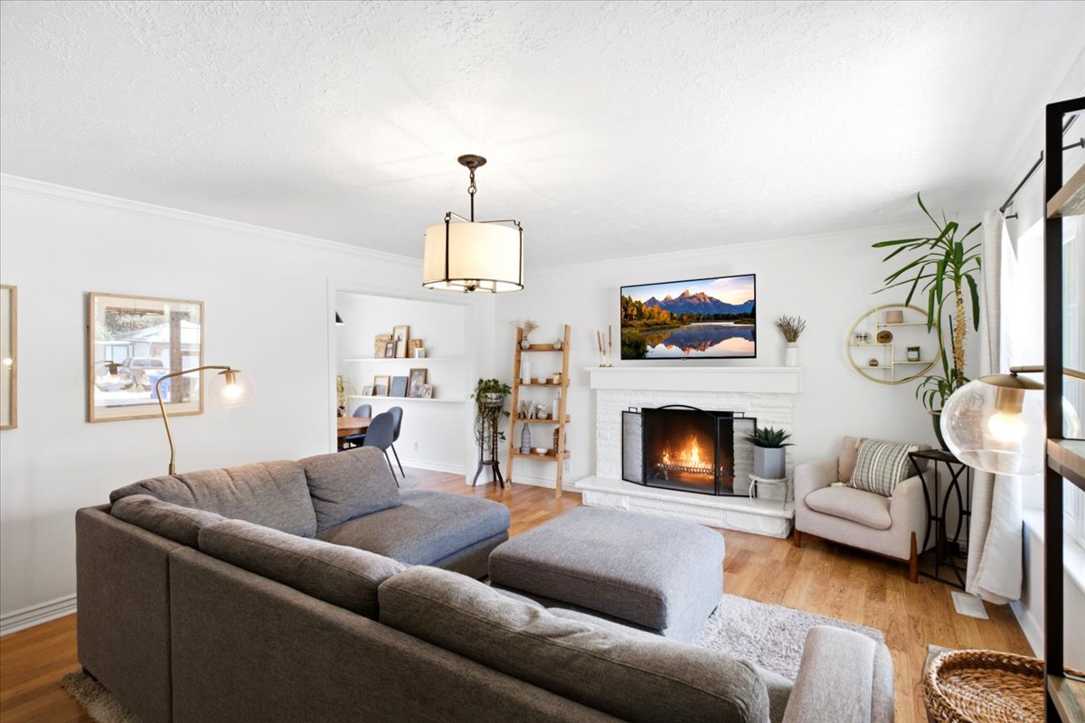 Living area featuring wood-finish flooring, a white brick fireplace with a mantel, and a drum pendant light fixture