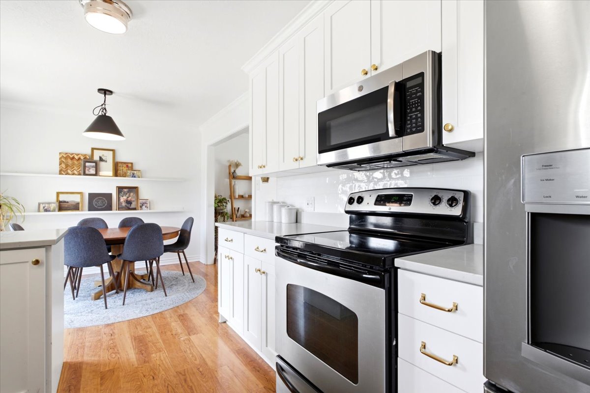 Bright kitchen featuring white shaker cabinetry, stainless steel appliances, light countertops, a white subway tile backsplash, and wood-finish flooring