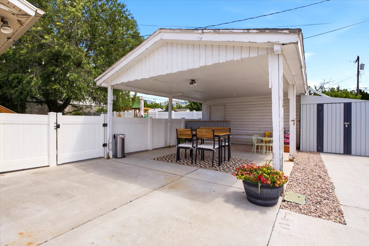 Covered patio area featuring a concrete slab, gravel border, and white vinyl fencing