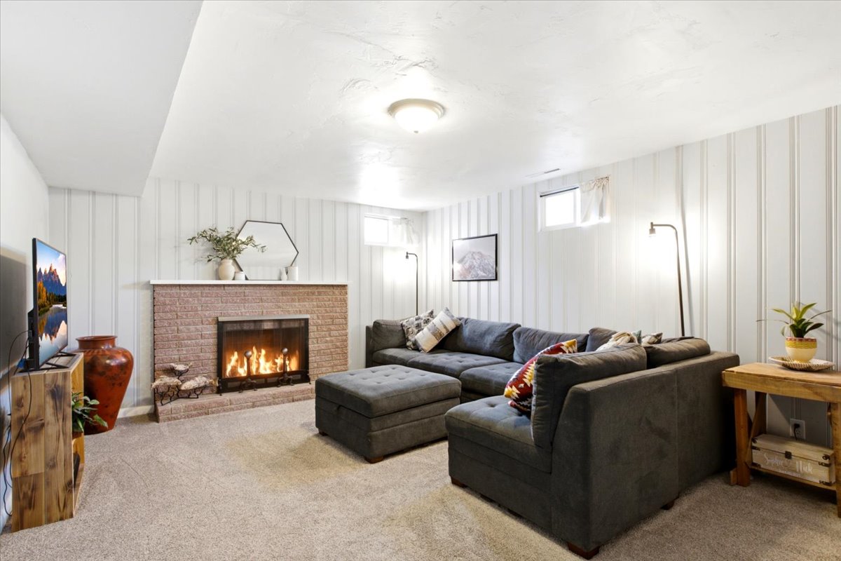 Living area featuring a brick-surround fireplace with a white mantel, light-toned carpet, and vertical plank wall paneling