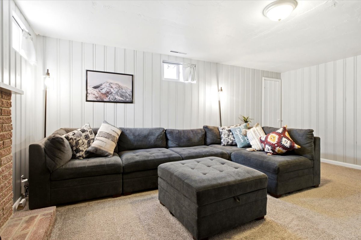 Spacious room featuring white vertical plank walls, light neutral carpeting, and a brick fireplace surround with a white mantel