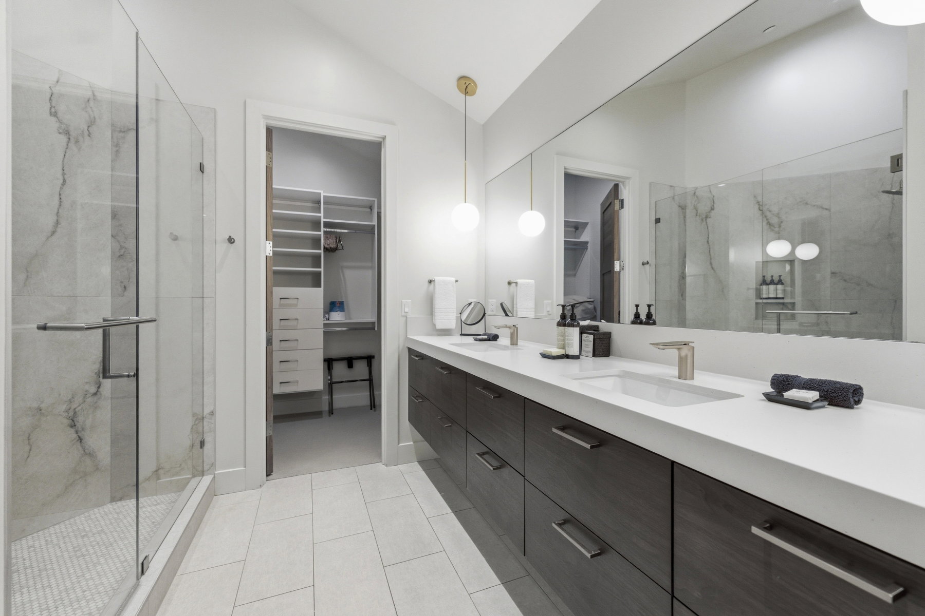 Modern bathroom featuring a double vanity with integrated sinks and dark wood-finish cabinetry, a large frameless mirror, and contemporary pendant lighting