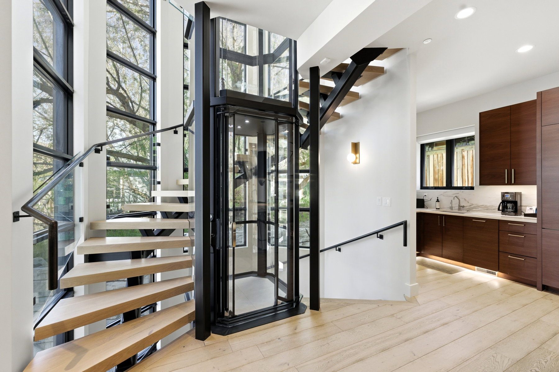 Multi-level living space featuring an integrated elevator, light wood-finish flooring, and a modern floating staircase with glass railing