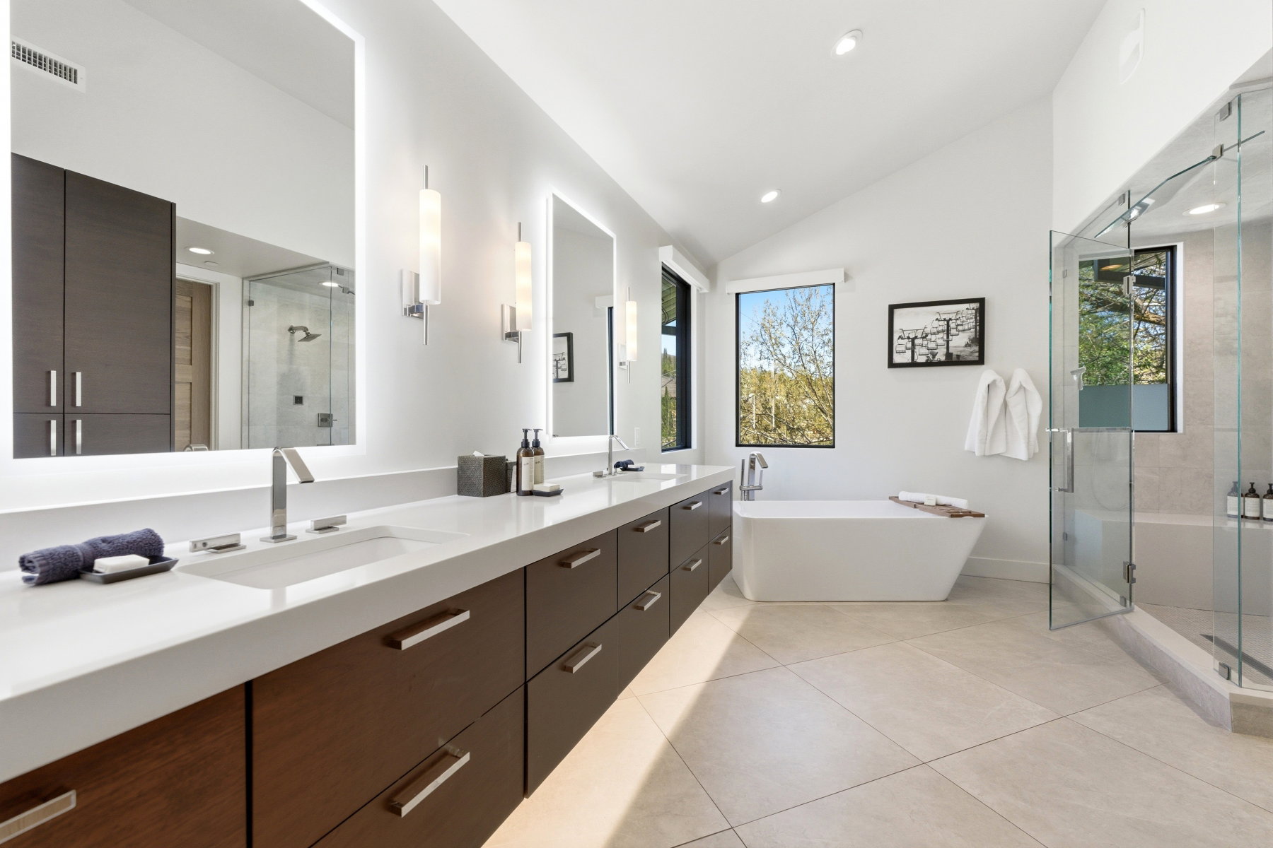Spacious bathroom featuring a dual vanity with integrated sinks, a freestanding soaking tub, a glass-enclosed shower, and vaulted ceilings