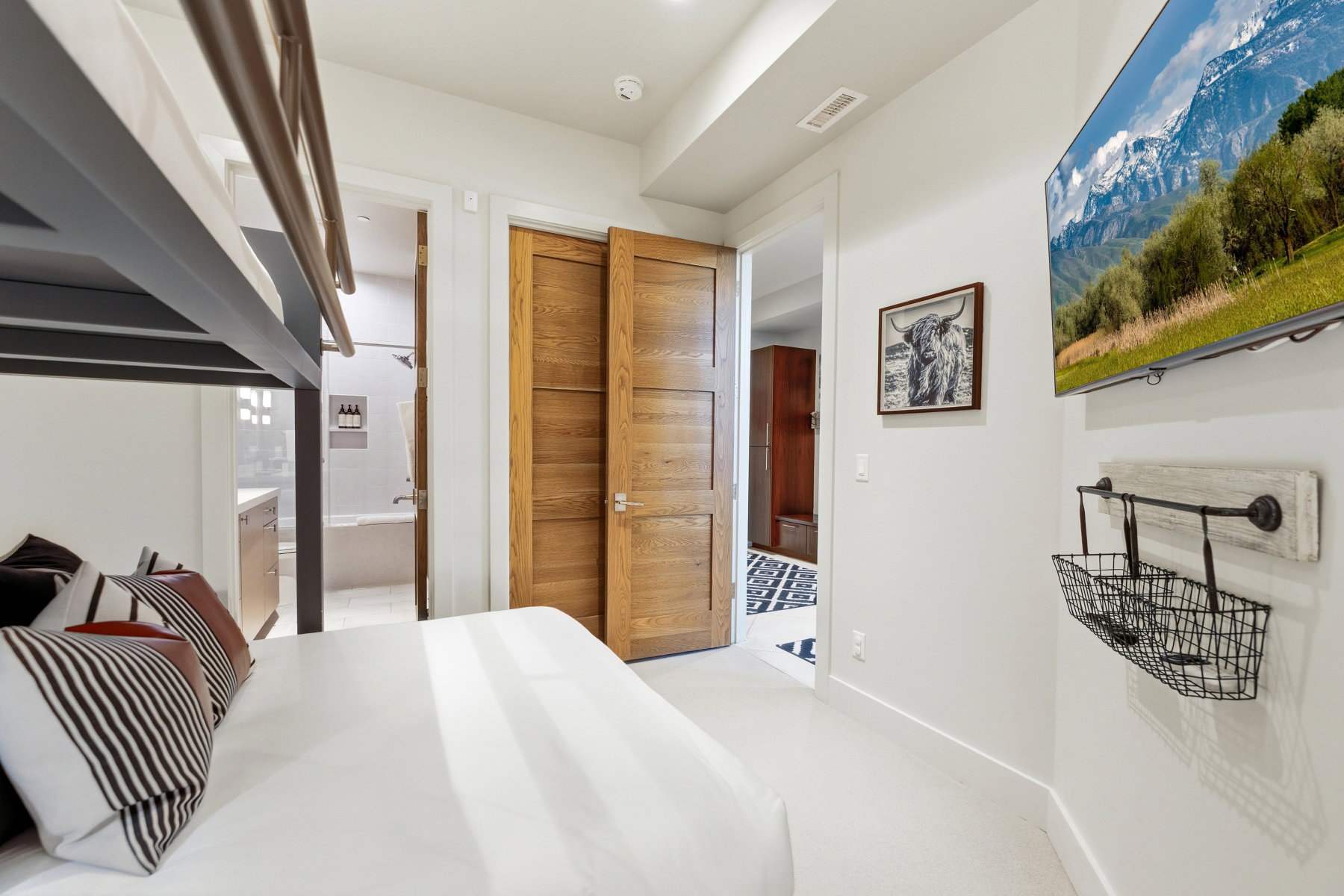 Bunk bedroom featuring a built-in bunk bed, wood-finish doors, wall-mounted television, and an adjacent bathroom with a tiled shower/tub combination and vanity