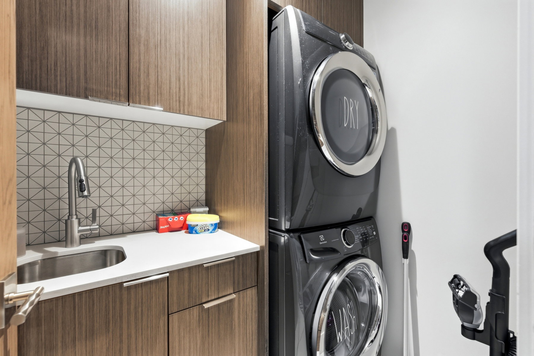Laundry area featuring stacked appliances, a stainless steel sink, and a geometric-patterned tile backsplash
