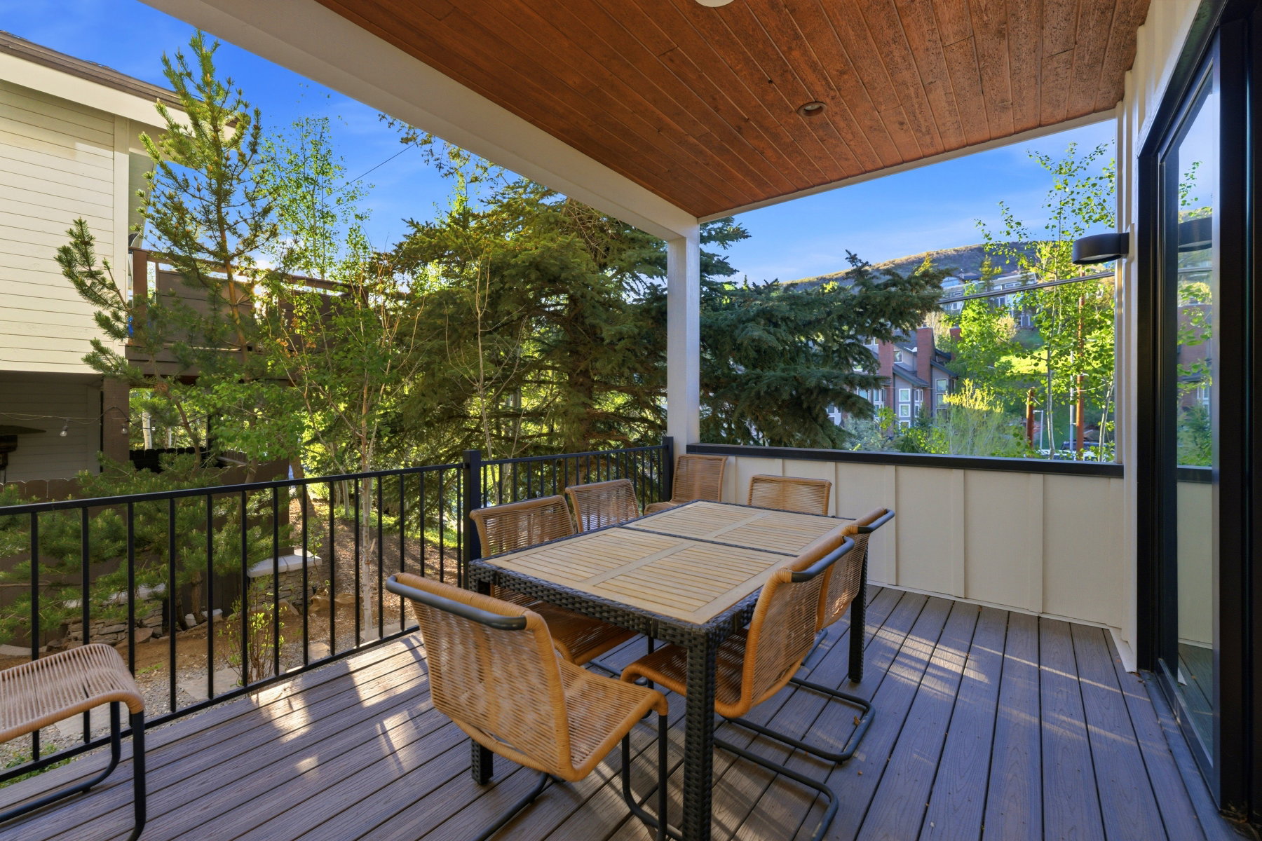 Covered outdoor deck with wood-finish ceiling, dark composite decking, and black metal railing