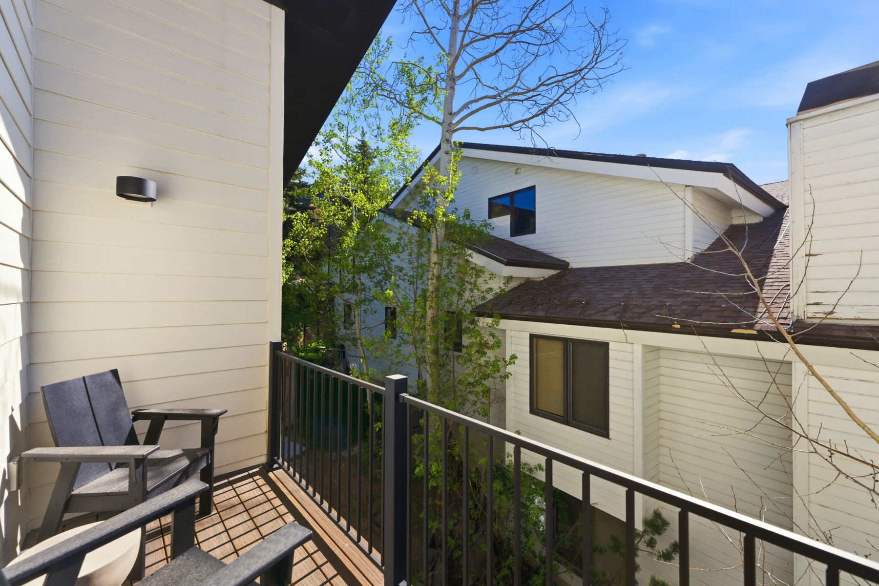 Private balcony featuring wood-finish decking, black metal railing, and a wall-mounted exterior light fixture