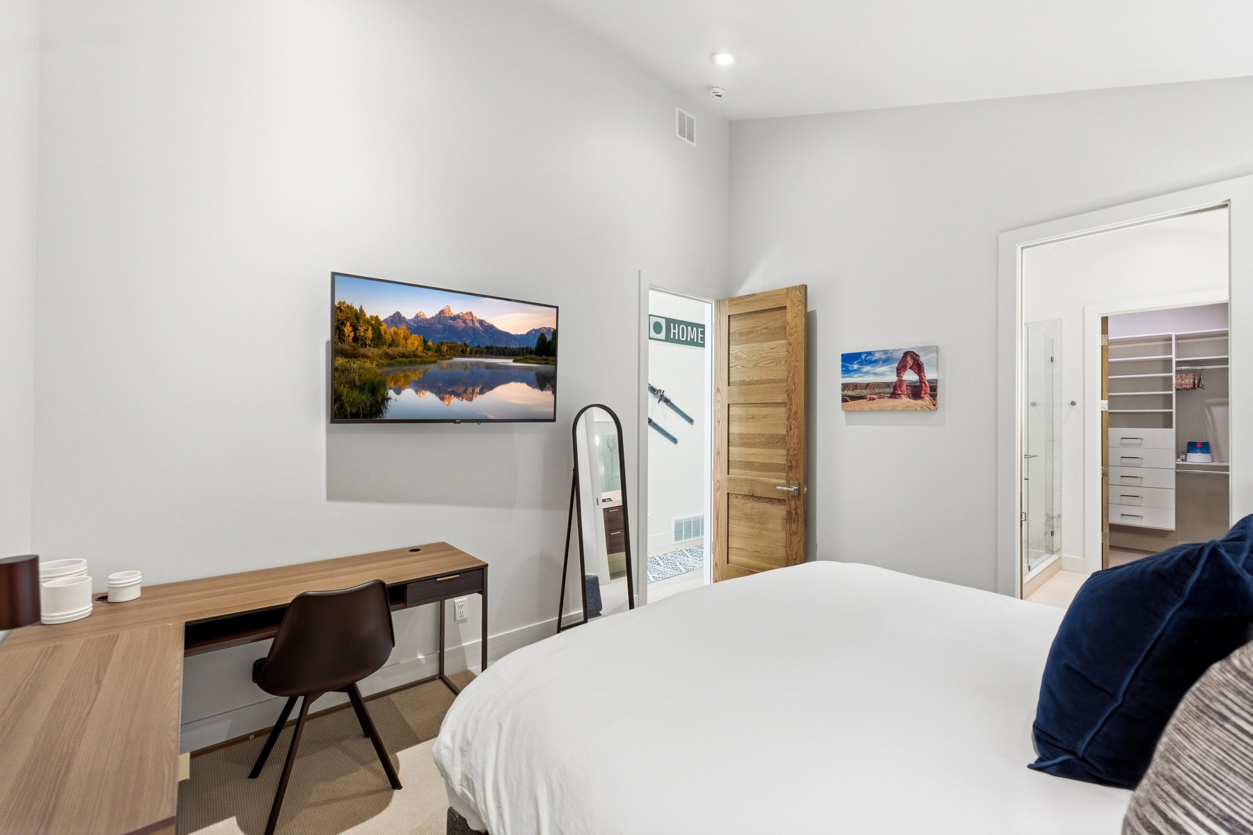 Bedroom featuring a wood-finish desk, wall-mounted television, and light-colored walls
