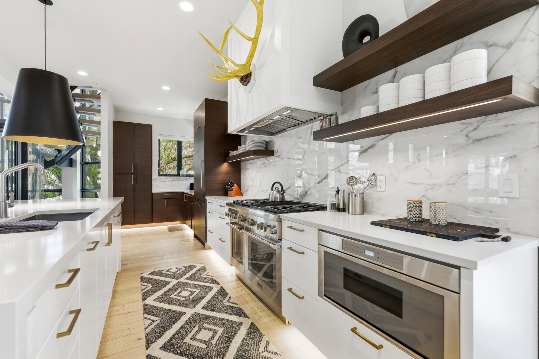 Modern kitchen featuring wood-finish flooring, white cabinetry with gold-toned hardware, and a large kitchen island with an undermount sink