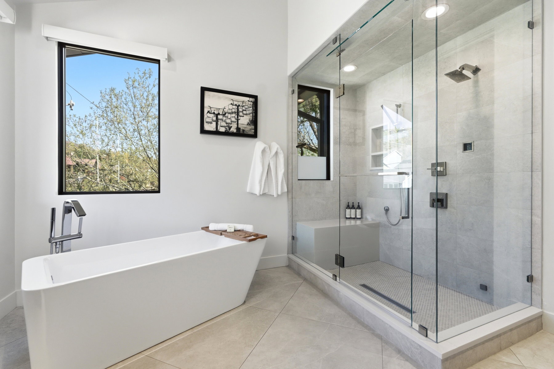 Modern bathroom featuring a freestanding soaking tub with floor-mounted faucet, an expansive glass-enclosed shower with a built-in bench, rainfall shower head, and wall-mounted fixtures