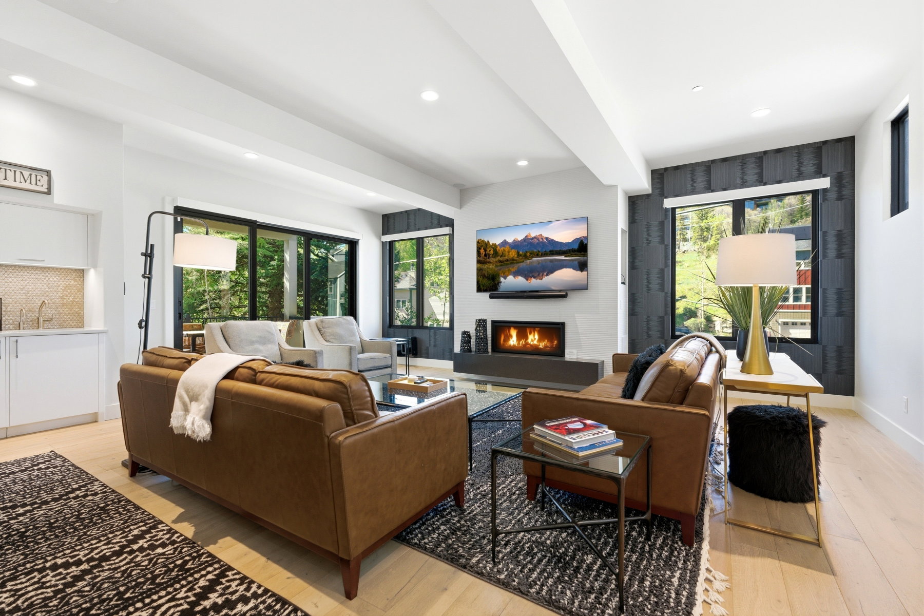 Spacious living area featuring light wood-finish flooring, recessed lighting, and a modern fireplace with a wall-mounted display