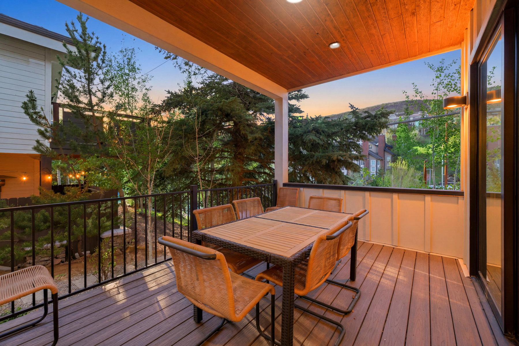 Covered outdoor deck featuring composite decking, black metal railings, a wood-finish ceiling, and an exterior wall light fixture