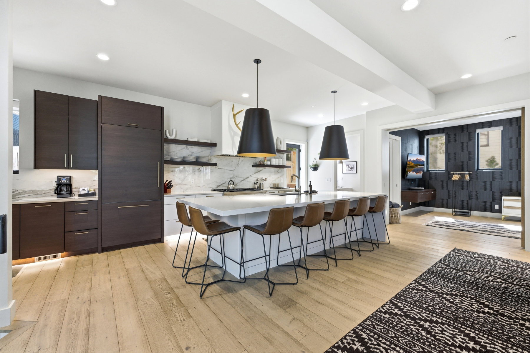 Contemporary kitchen featuring a large central island, light wood-finish flooring, dark wood cabinetry, integrated appliances, and a marble-patterned backsplash