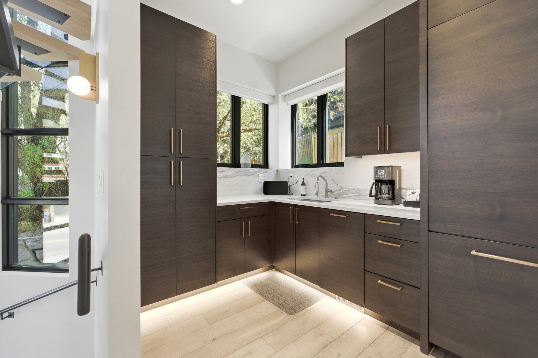 Contemporary kitchen featuring dark wood-finish cabinetry with gold-tone hardware, white marble-style countertops, and light wood-finish flooring