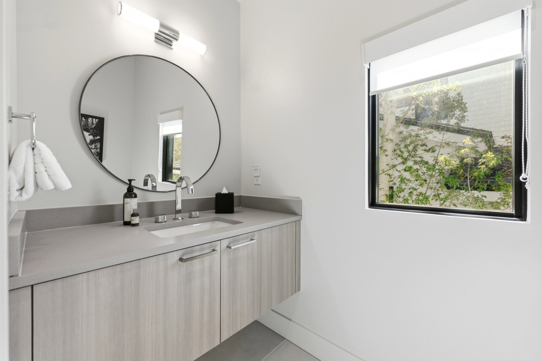 Bathroom featuring a floating vanity with wood-finish cabinetry, an integrated sink, and a large circular mirror