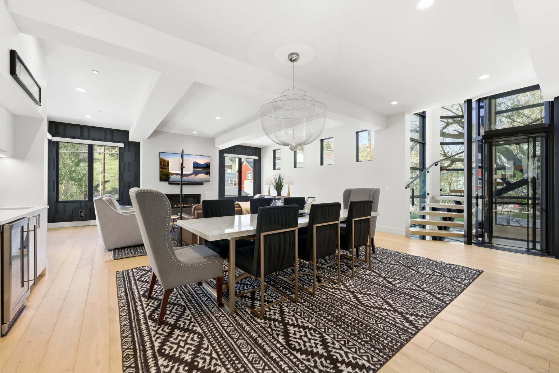 Open-concept living area featuring light wood-finish flooring, recessed lighting, a modern chandelier, a built-in electric fireplace, and a glass-enclosed staircase