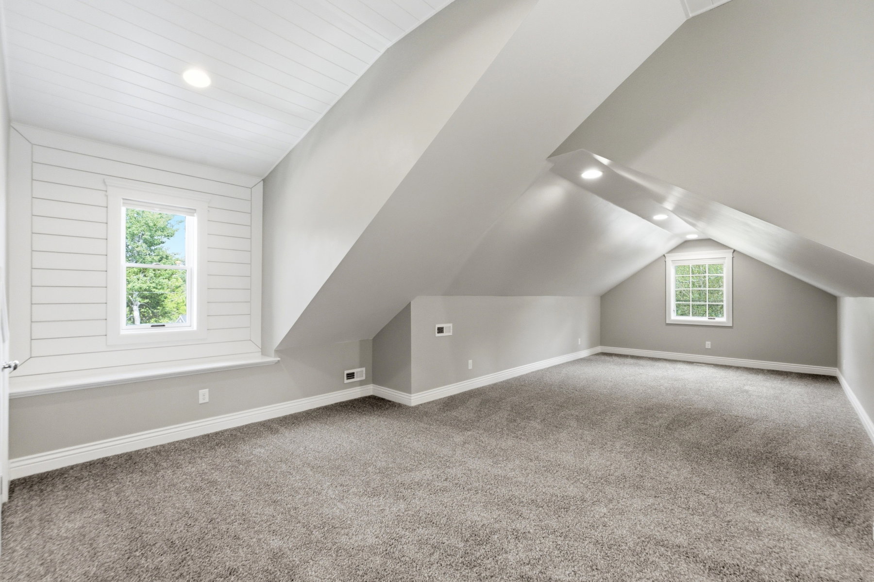 Carpeted room featuring a white shiplap accent wall, multiple windows, recessed lighting, and sloped ceilings