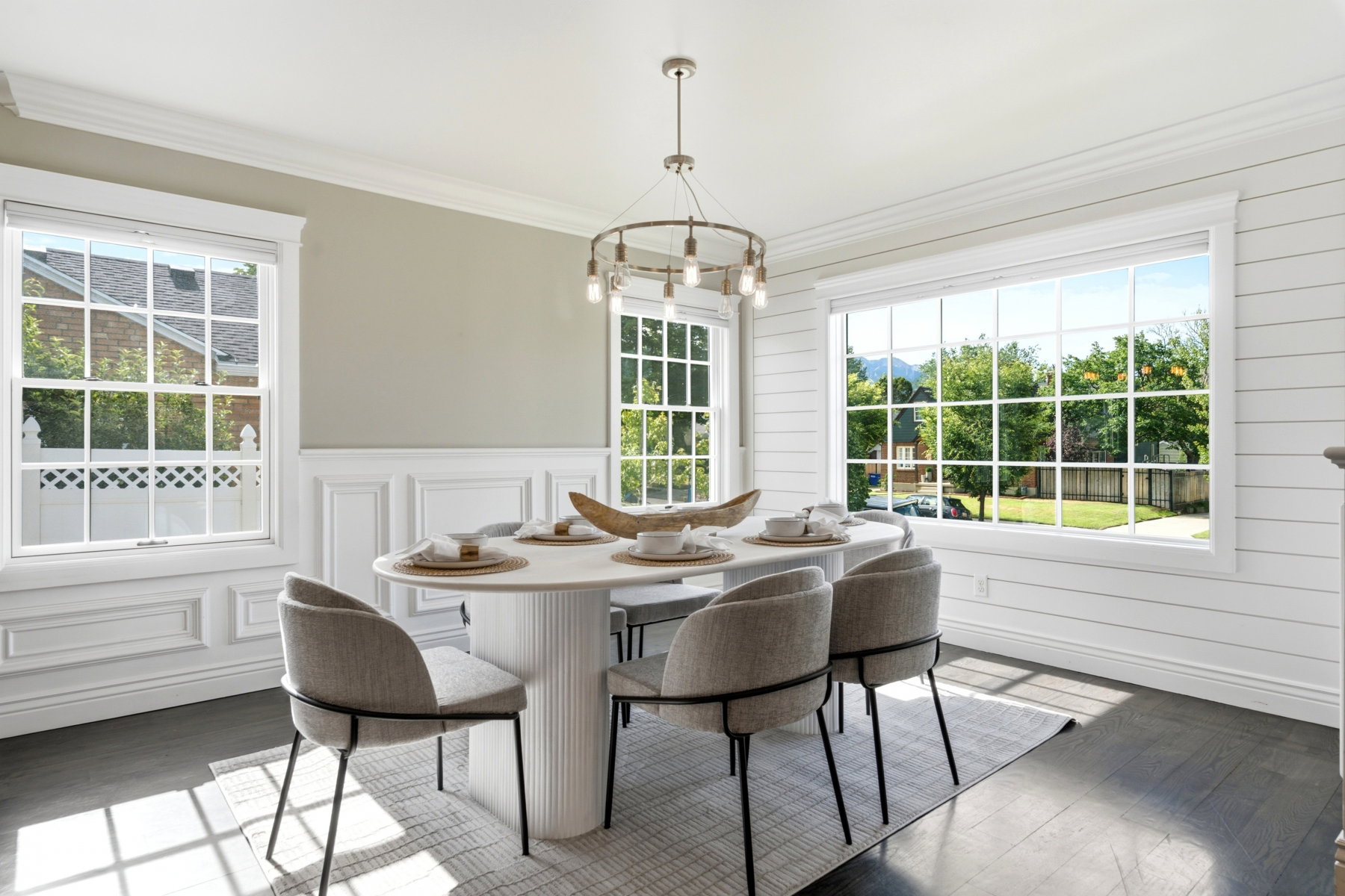 Spacious dining area featuring large windows, wood-finish flooring, white shiplap wall accents, traditional wainscoting, and a contemporary chandelier