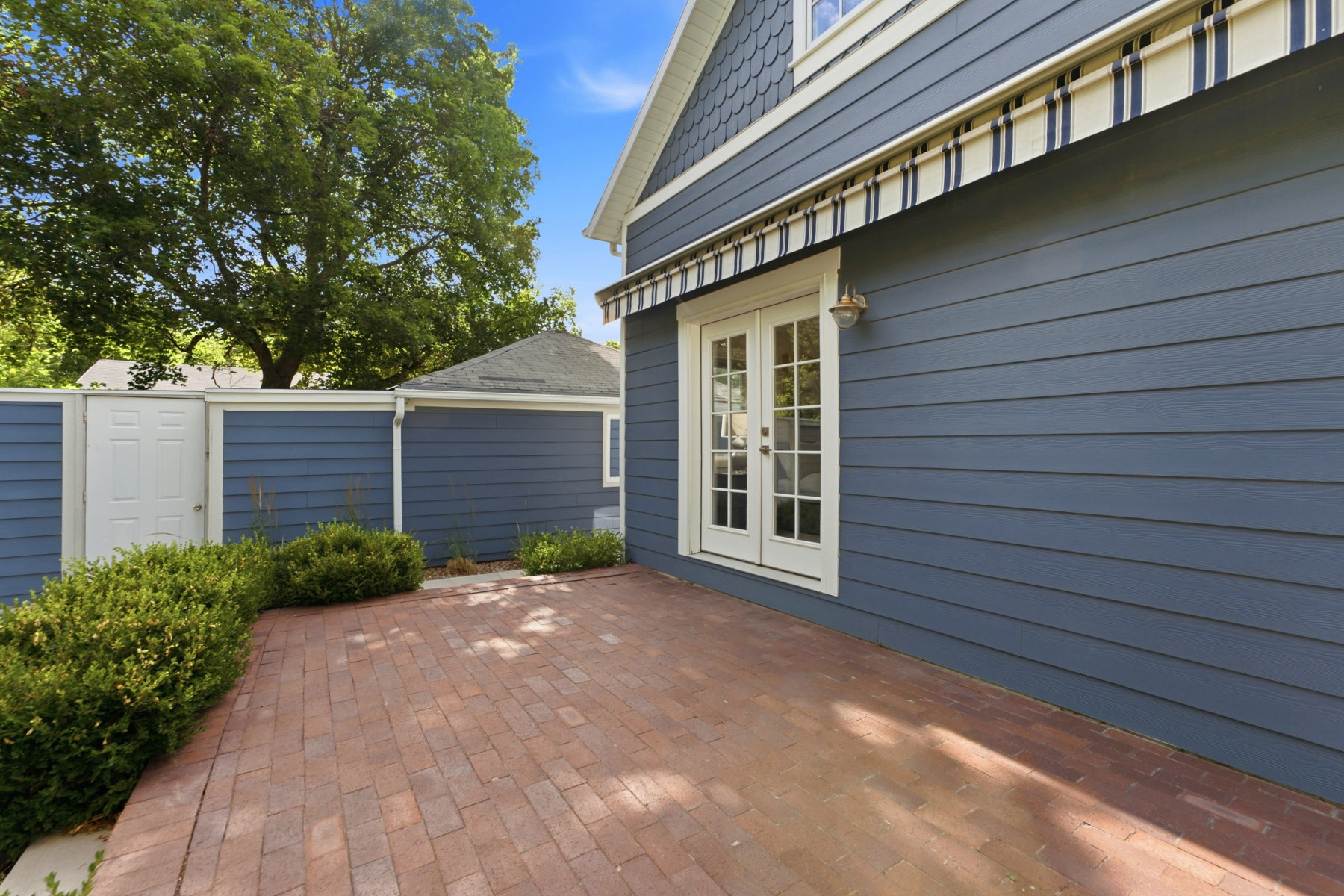 Brick paver patio with a striped retractable awning and white French doors