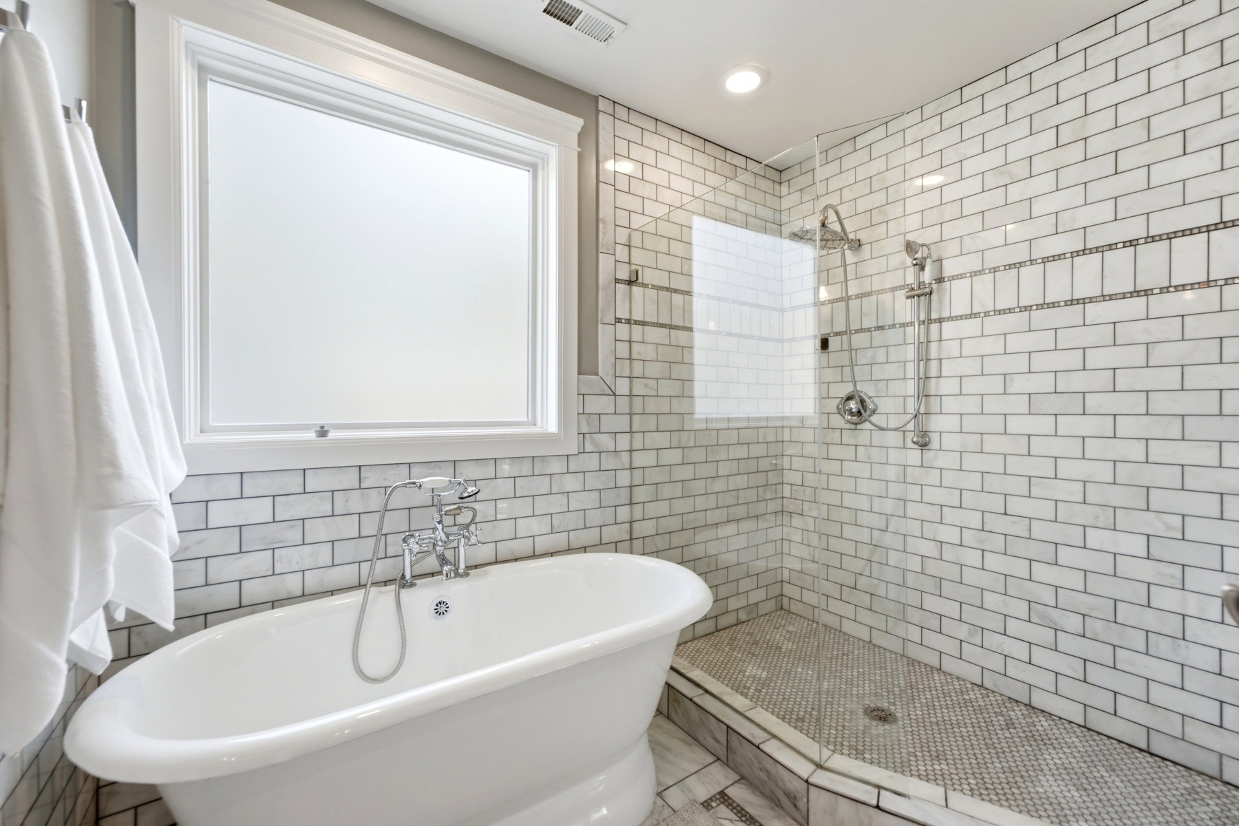 Bathroom featuring a freestanding soaking tub, a separate walk-in shower with clear glass enclosure, and white subway tile surround with decorative accent bands
