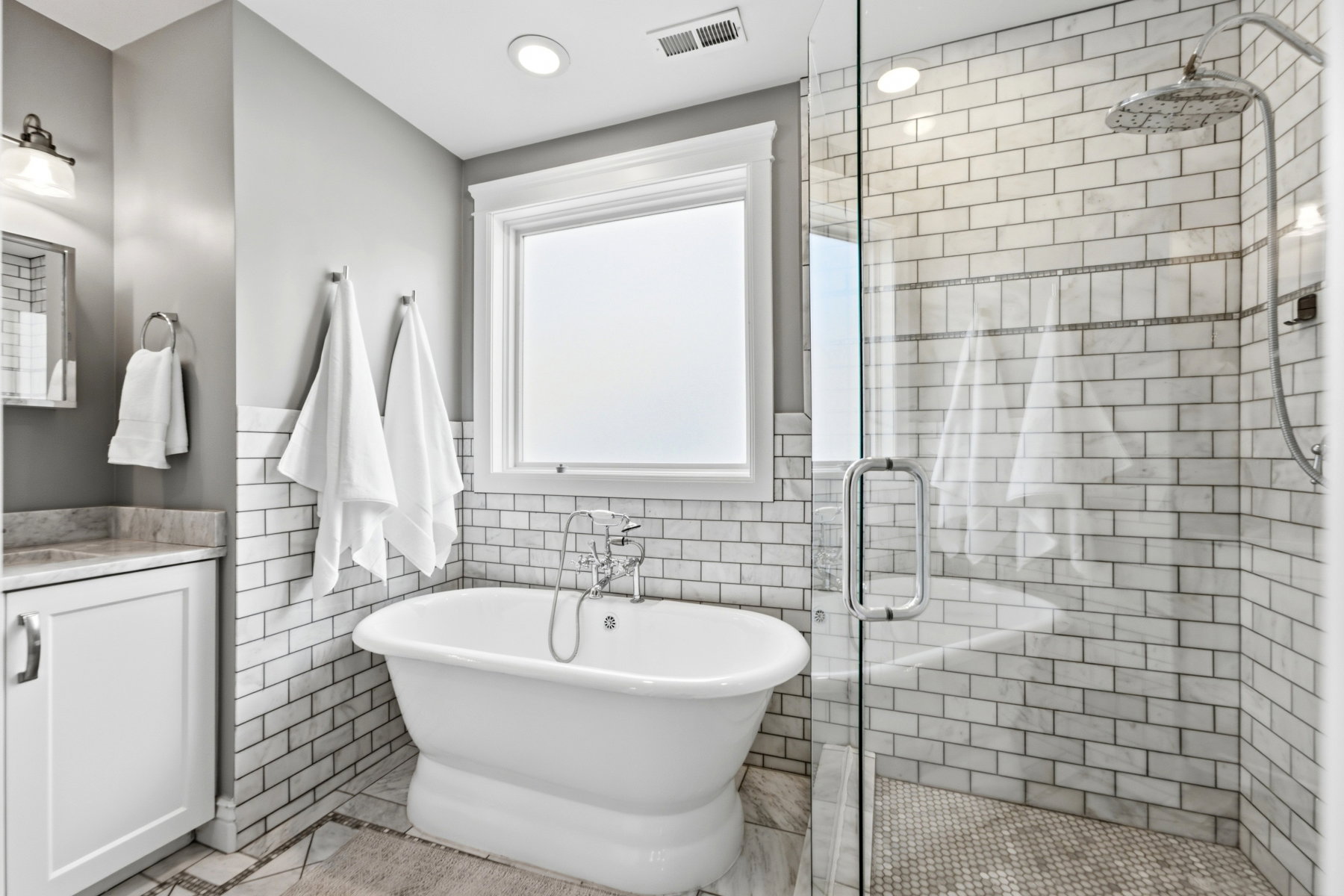 White subway tile wainscoting and a freestanding soaking tub anchor this refined bathroom